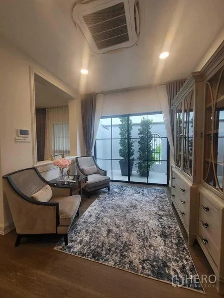Detached House for rent in Saphan Sung, Bangkok - Sitting nook with two armchairs, display cabinet and sliding doors to a terrace.