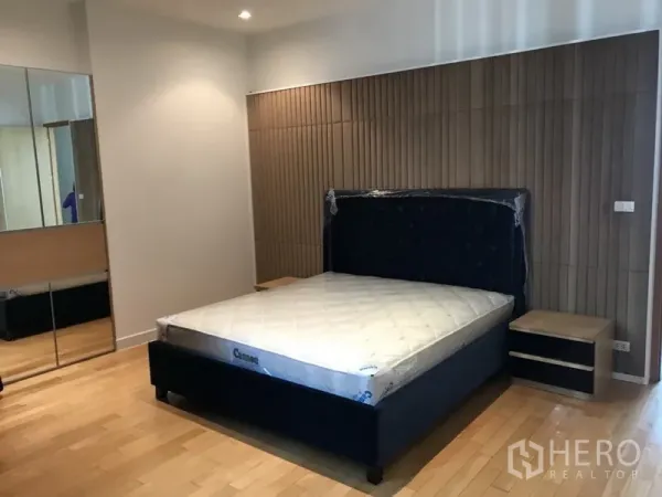 Condominium for rent in Khlong Toei, Bangkok - Spacious master bedroom with upholstered bed, mirrored wardrobe and wood-slat feature wall.