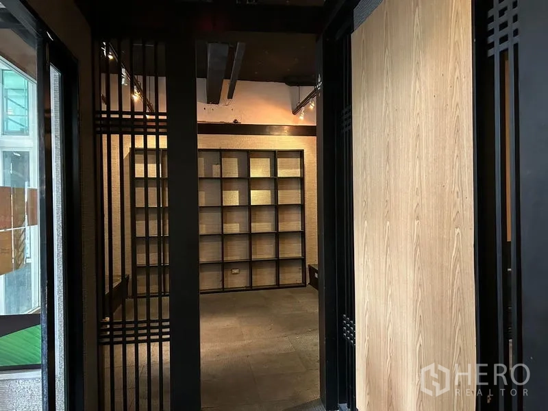 零售空间 出租在Bang Rak, Bangkok - 入口走廊通向展示间，整面墙网格陈列架与射灯轨道。