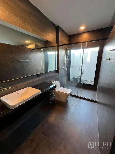 独立式住宅 出租或出售在Bang Phli, Samut Prakan - 现代卫浴，长台面洗手台、玻璃淋浴间与深色瓷砖。