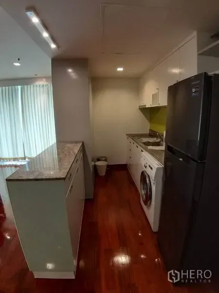 Condominium for rent or sale in Pathum Wan, Bangkok - Galley kitchen featuring granite countertop, white cabinetry and an in-unit washing machine.