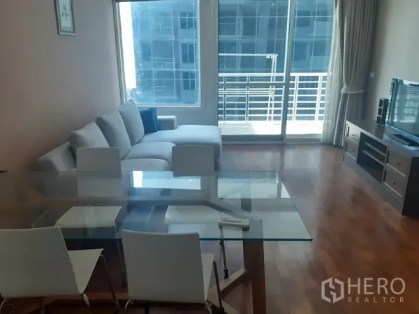 Condominium for rent in Khlong Toei, Bangkok - Living room with L-shaped sofa, glass dining table, TV console, and sliding doors to a balcony with city views.