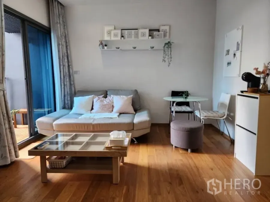 Condominium for rent in Watthana, Bangkok - Bright living room with sofa, glass coffee table and sliding doors to the balcony in a 1-bedroom condo near BTS Nana.