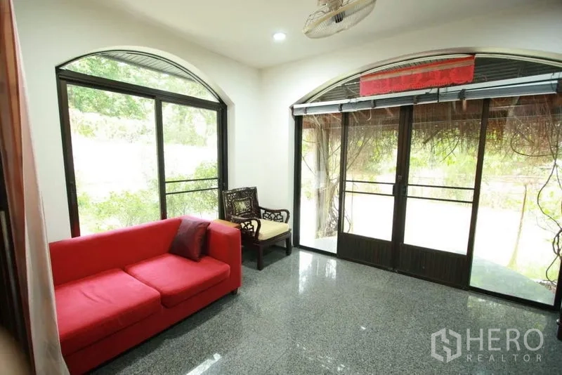 独立式住宅 出租在Bang Phli, Samut Prakan - 明亮起居角，红色沙发与拱形推拉门通向花园。