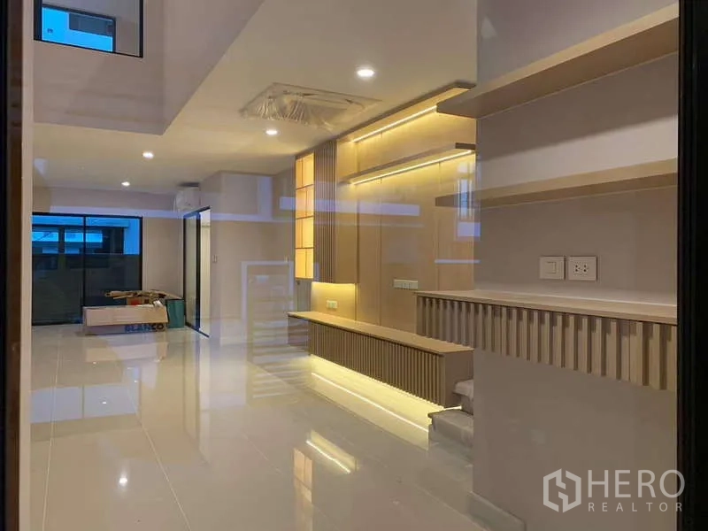 Townhouse for rent or sale in Saphan Sung, Bangkok - Open-plan living area with glossy tile floor, backlit feature wall and sliding glass doors.