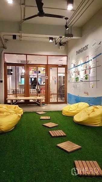 店屋 出租在Pathum Wan, Bangkok - 室内花园式休闲区，人造草坪、黄色懒人沙发、木质踏步与玻璃会议室及地图墙。