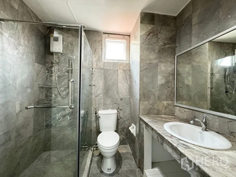 Townhouse for rent or sale in Suan Luang, Bangkok - Bright bathroom with gray marble tiles, glass shower, and long vanity mirror