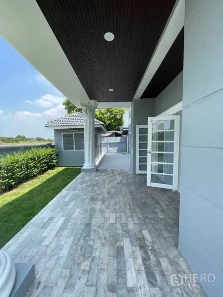 บ้าน ขายในBang Na, Bangkok - ระเบียงหน้าบ้านมุงหลังคาปูหิน เสาโรมัน ประตูบานฝรั่งเศส ข้างสนามหญ้าเรียบสวย