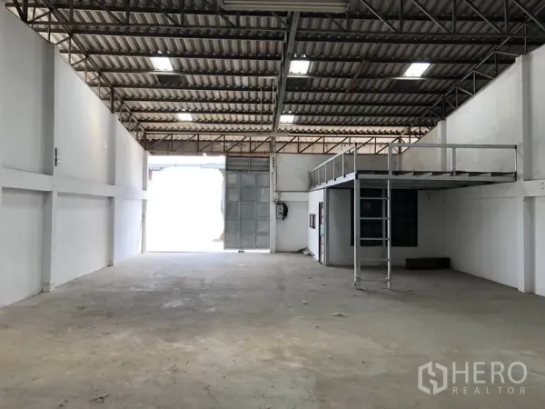 Warehouse for rent or sale in Khlong Luang, Pathum Thani - Open warehouse facing a large sliding entry door, with mezzanine and small office, high ceiling and concrete flooring for storage.