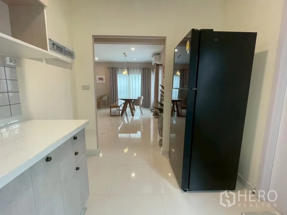 บ้านเดี่ยว for rent in Bang Phli, Samut Prakan - ทางเชื่อมครัวมีตู้เย็นสีดำ มองออกไปยังโซนรับประทานอาหาร.