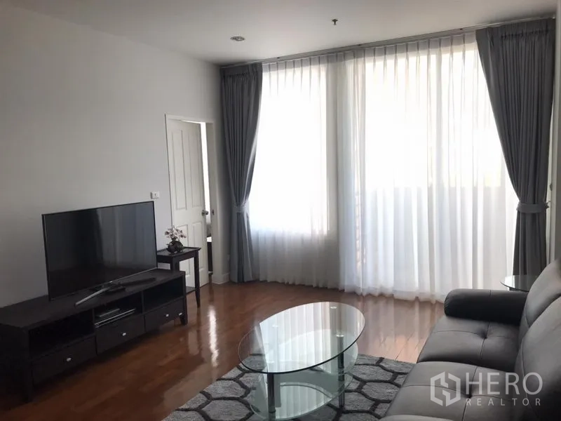 Condominium for rent in Khlong Toei, Bangkok - Bright living room with floor-to-ceiling curtains, TV console, glass coffee table, sofa and hardwood floors.