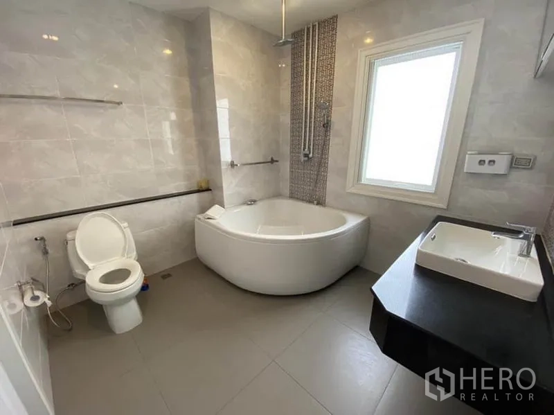 Townhouse for rent in Bang Na, Bangkok - Bathroom with corner soaking tub, rain shower, vanity, and window.