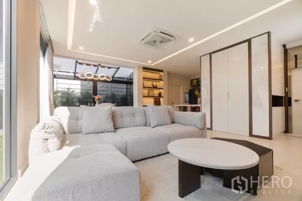 Detached House for rent or sale in Prawet, Bangkok - Bright living room with large sofa, built-in shelves and view to glass dining area