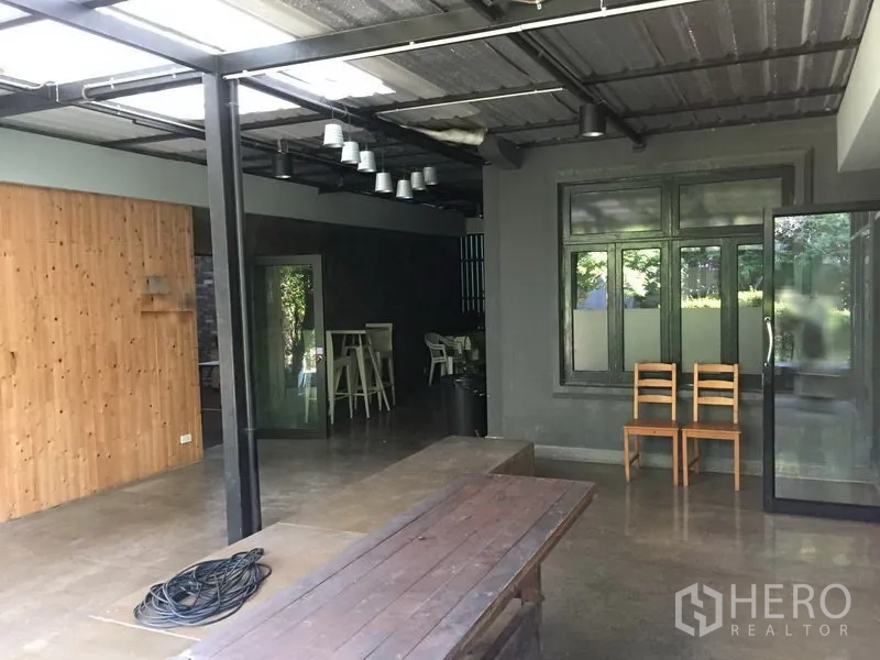 办公空间 出租在Khlong Toei, Bangkok - 半户外工作区，金属屋顶、木质墙面与玻璃门，配长条木桌