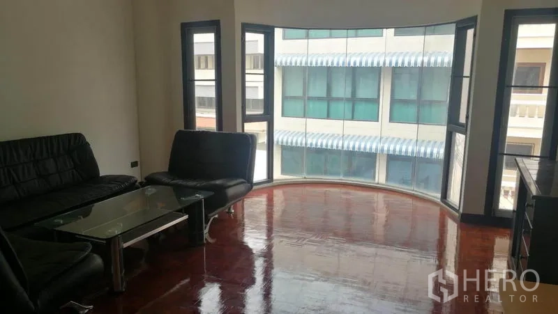 Townhouse for rent in Khlong Toei, Bangkok - Living room with curved bay window, black leather sofas and glass coffee table.