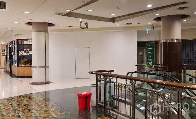 Retail Space for rent - Shopping mall corridor with a vacant white shopfront beside an escalator railing and polished floors.
