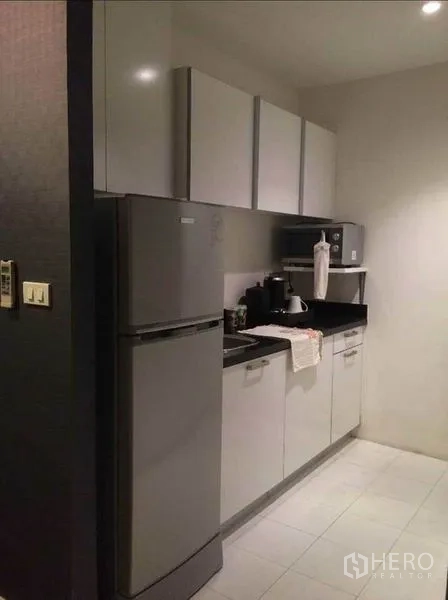 公寓 出售在Pathum Wan, Bangkok - 走廊式厨房，带冰箱、白色橱柜和黑色台面。