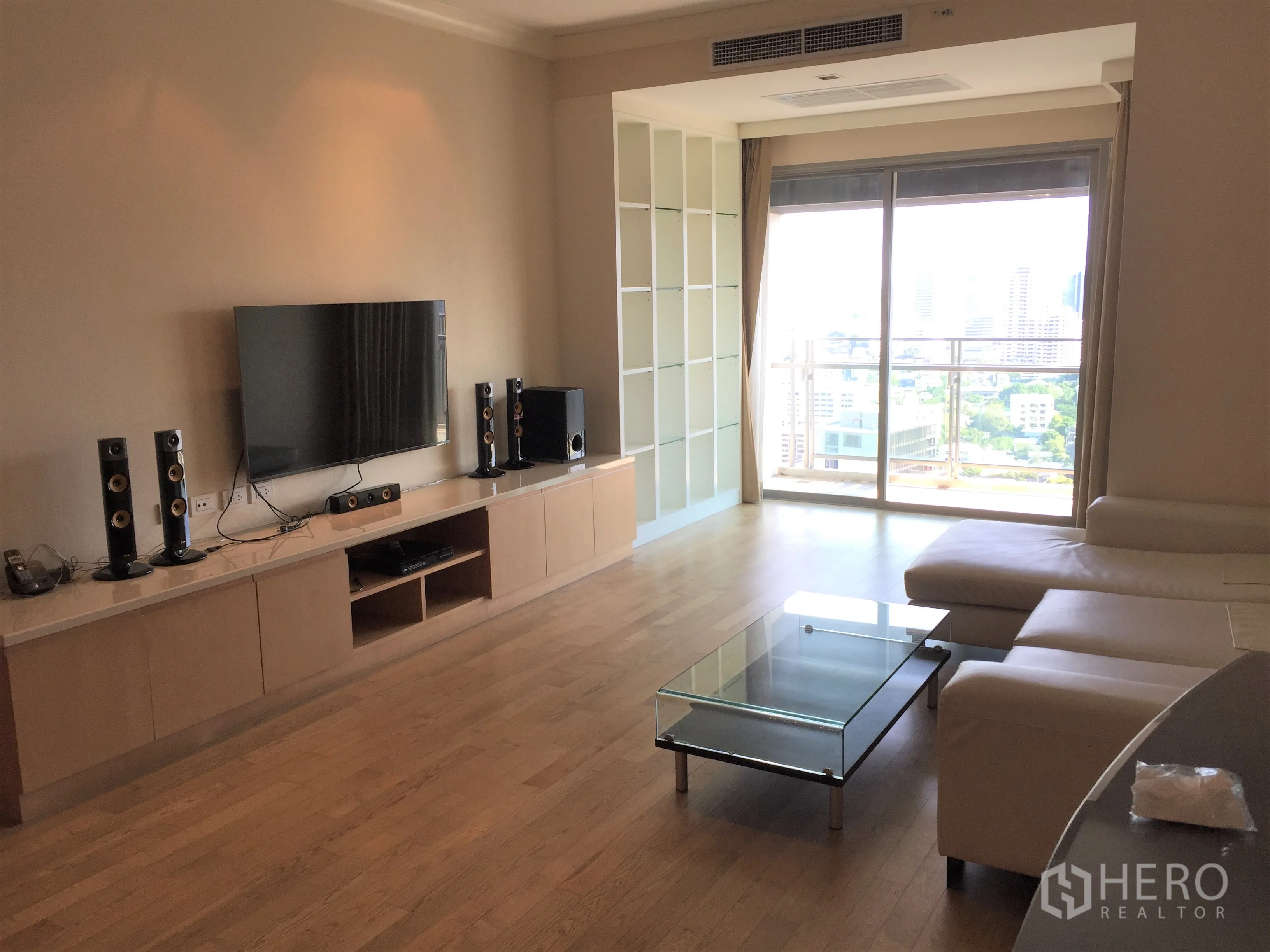 公寓 出租在Watthana, Bangkok - 宽敞客厅，墙挂电视与影音柜，玻璃茶几，阳台可赏城市景观。