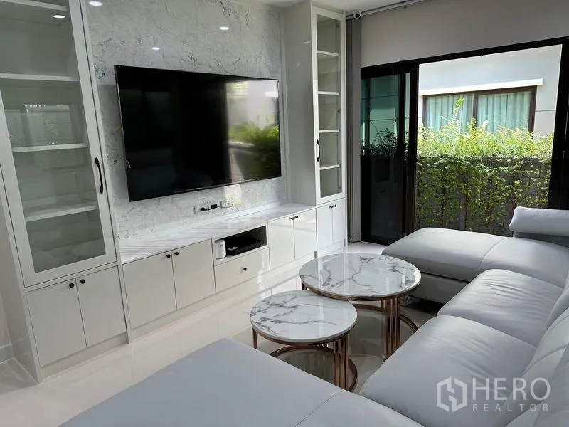 Detached House for sale in Saphan Sung, Bangkok - Living room with marble TV wall, glass cabinets and sliding doors to the garden.