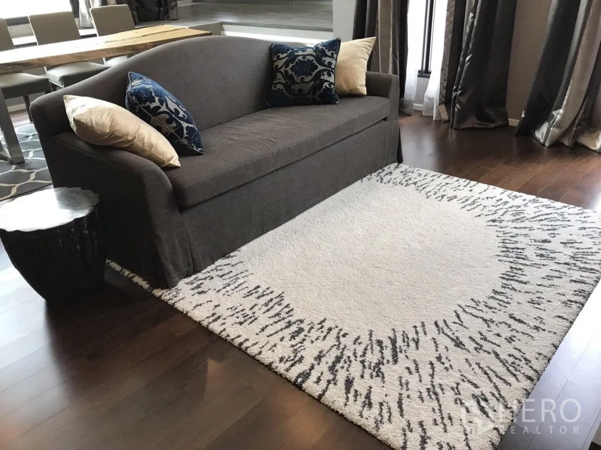 Condominium for rent or sale in Huai Khwang, Bangkok - Living room featuring a gray sofa, accent cushions and a patterned area rug on wooden flooring.