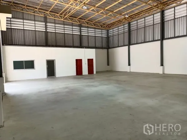 Warehouse for rent in Suan Luang, Bangkok - Large warehouse bay with truss roof, white partitioned office, and two red service doors.