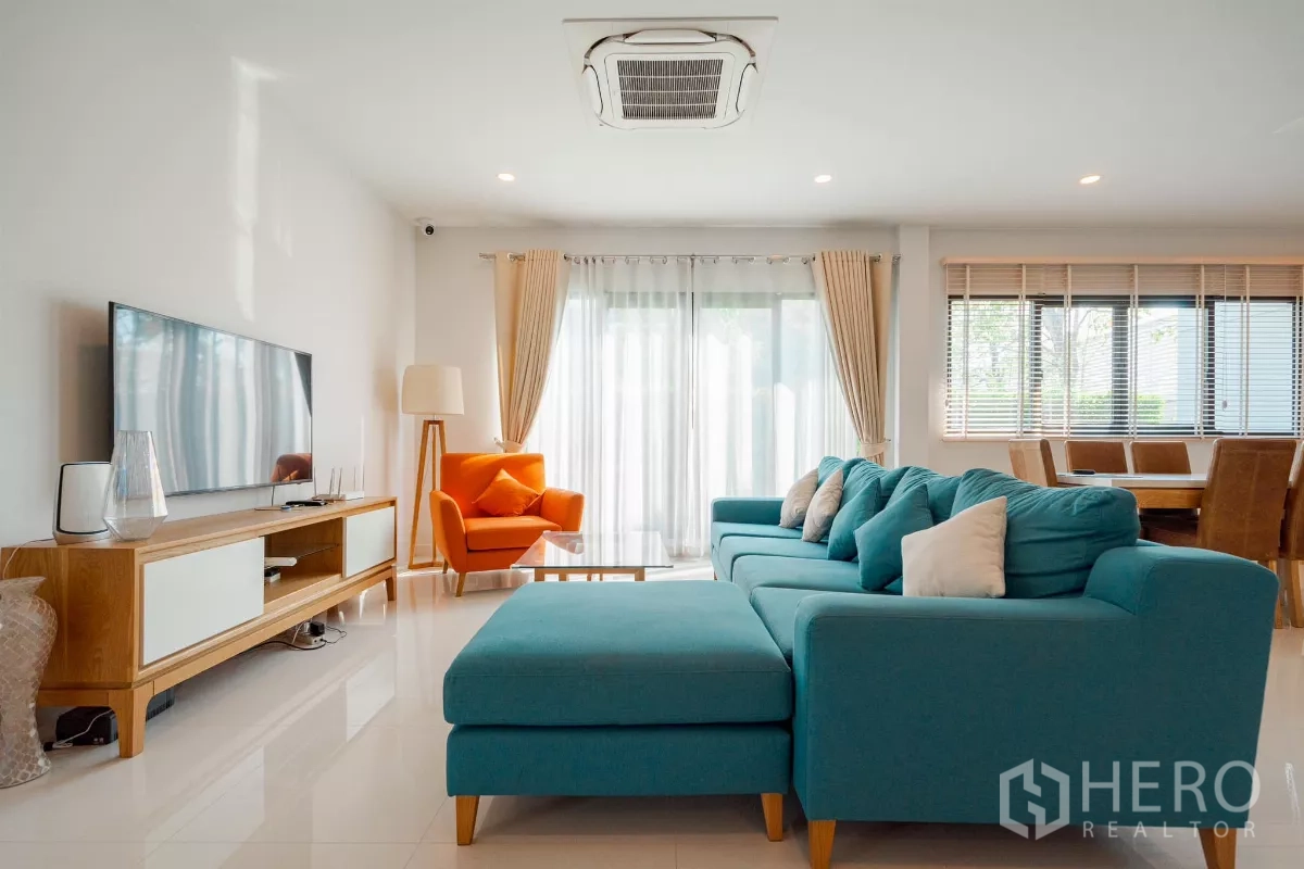 Detached House for sale in Saphan Sung, Bangkok - Family lounge with teal sectional sofa, orange armchair and TV console.