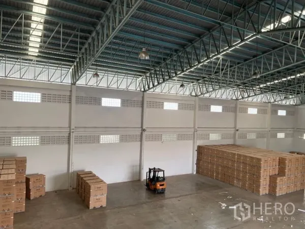 Warehouse for rent in Lat Krabang, Bangkok - Wide warehouse floor seen from above with a forklift and palletized boxes beneath skylights.