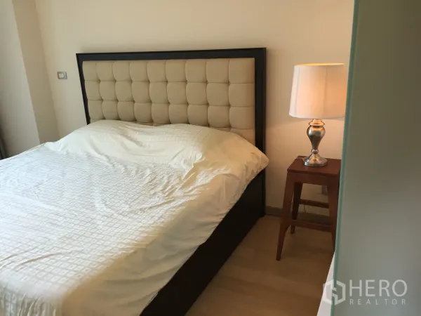 Condominium for rent or sale in Watthana, Bangkok - Primary bedroom with upholstered headboard bed and bedside lamp in warm neutral tones.