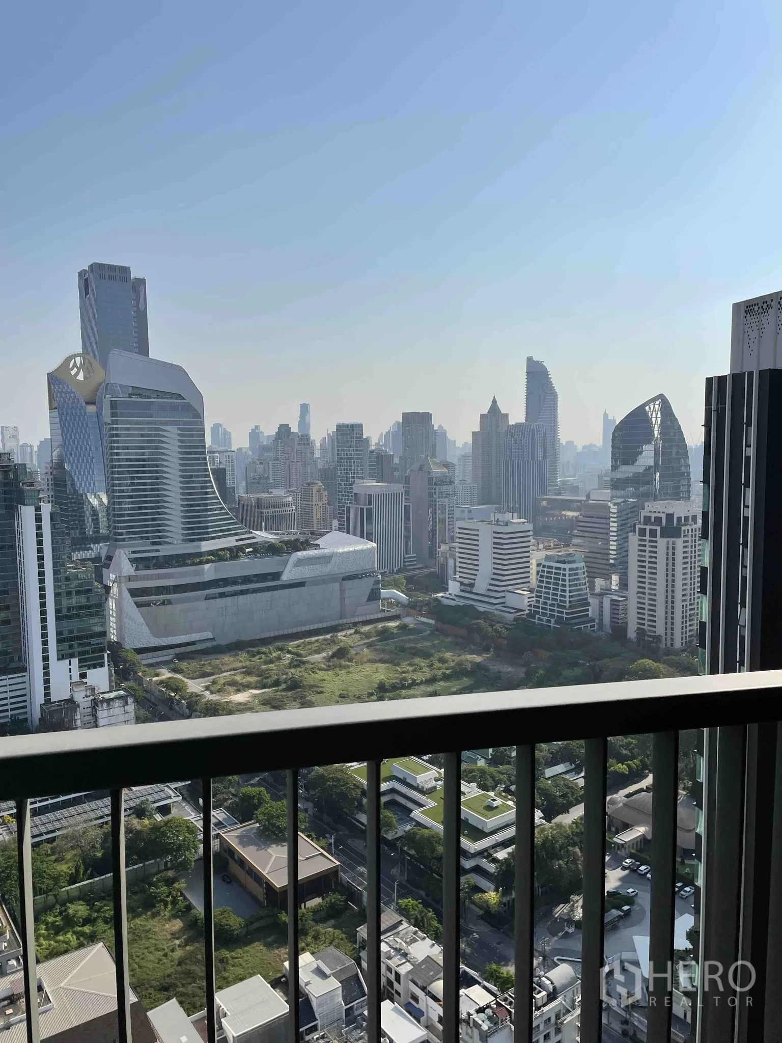 公寓 for rent in Pathum Wan, Bangkok - 阳台栏杆框景，俯瞰曼谷城市天际线与下方绿地。