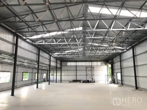 Warehouse for rent in Nonthaburi - Spacious warehouse interior with high steel truss roof, skylights and smooth concrete floor.