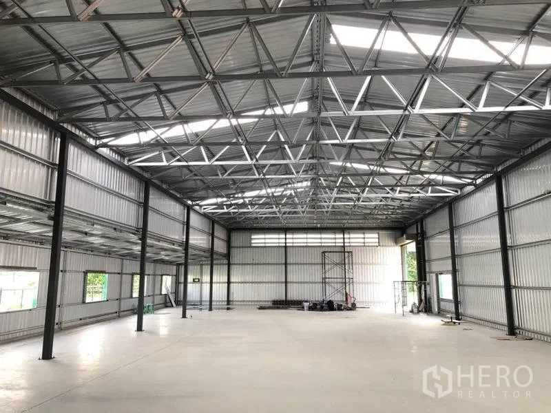 Warehouse for rent in Nonthaburi - Spacious warehouse interior with high steel truss roof, skylights and smooth concrete floor.
