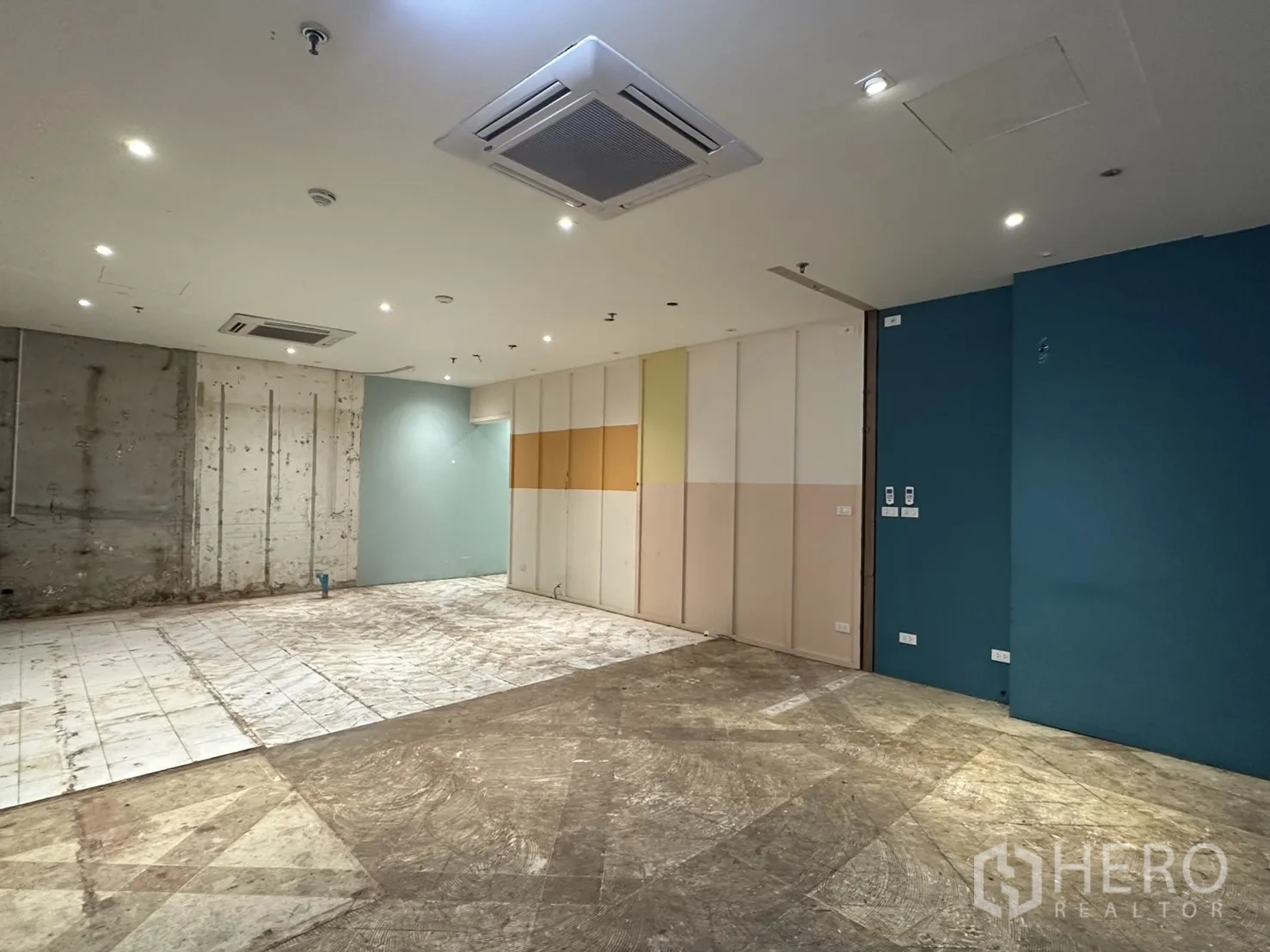 零售空间 for rent in Watthana, Bangkok - 开放式铺位另一角度，可见天花空调、射灯、彩色面板墙与混凝土墙。