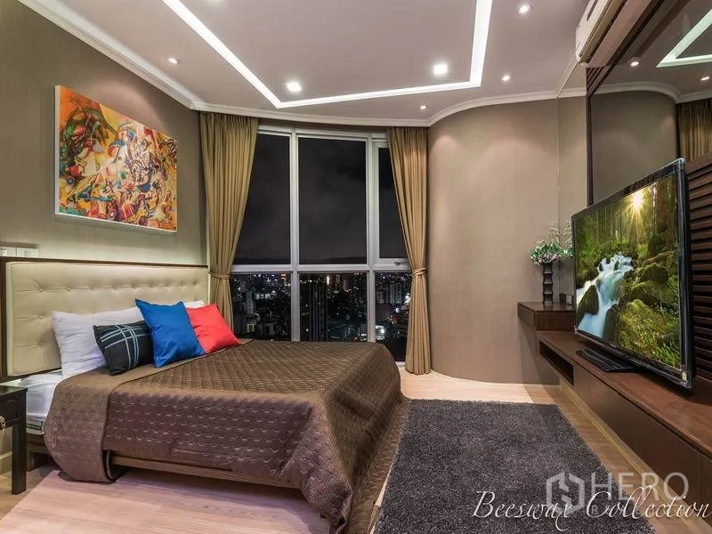 Condominium for rent in Watthana, Bangkok - Second bedroom featuring large curved window, cove lighting, wall‑mounted TV and colorful artwork.