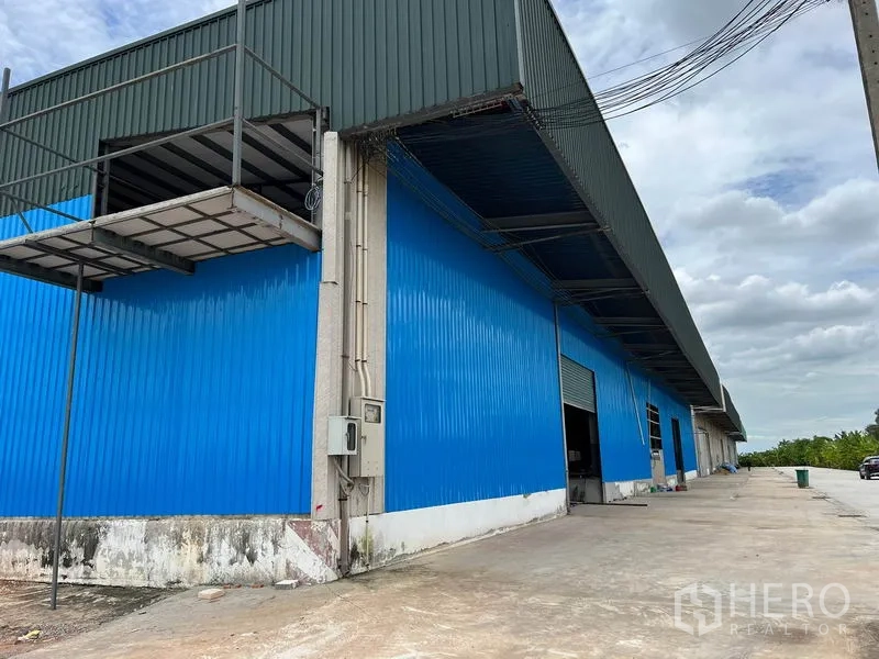 货栈 出租在Lat Krabang, Bangkok - 蓝色金属外墙仓库外观，带雨棚装卸区与宽阔混凝土场地。