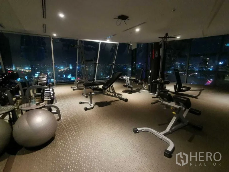 Condominium for rent in Ratchathewi, Bangkok - Fitness room with weights and machines overlooking city lights.