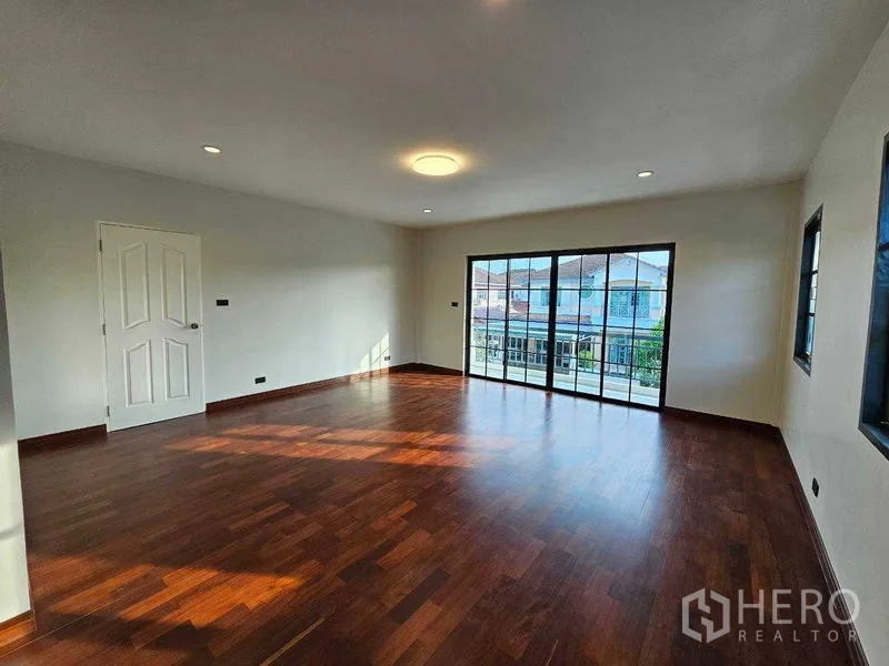Detached House for sale in Thanyaburi, Pathum Thani - Large master bedroom with wood flooring and wide sliding glass doors.