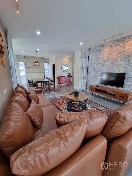 Detached House for rent or sale in Prawet, Bangkok - Open-plan living and dining area with leather sofa, TV and feature wall.
