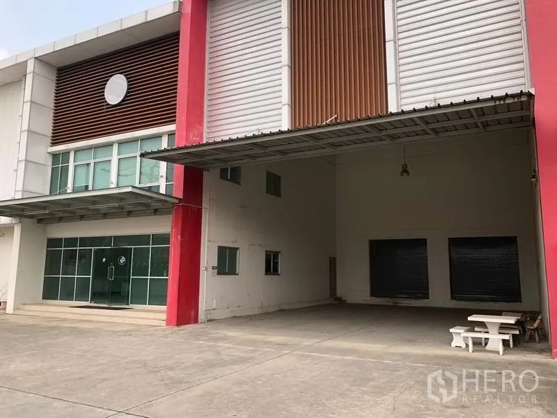 Factory for rent in Bang Sao Thong, Samut Prakan - Covered loading zone with high roller shutters and wide concrete yard.