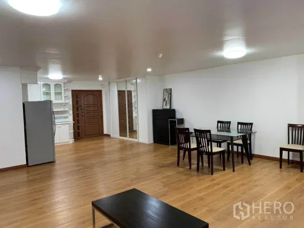 Condominium for rent or sale in Watthana, Bangkok - Open living space with dining set, mirrored wall, and wood flooring beside the kitchen.
