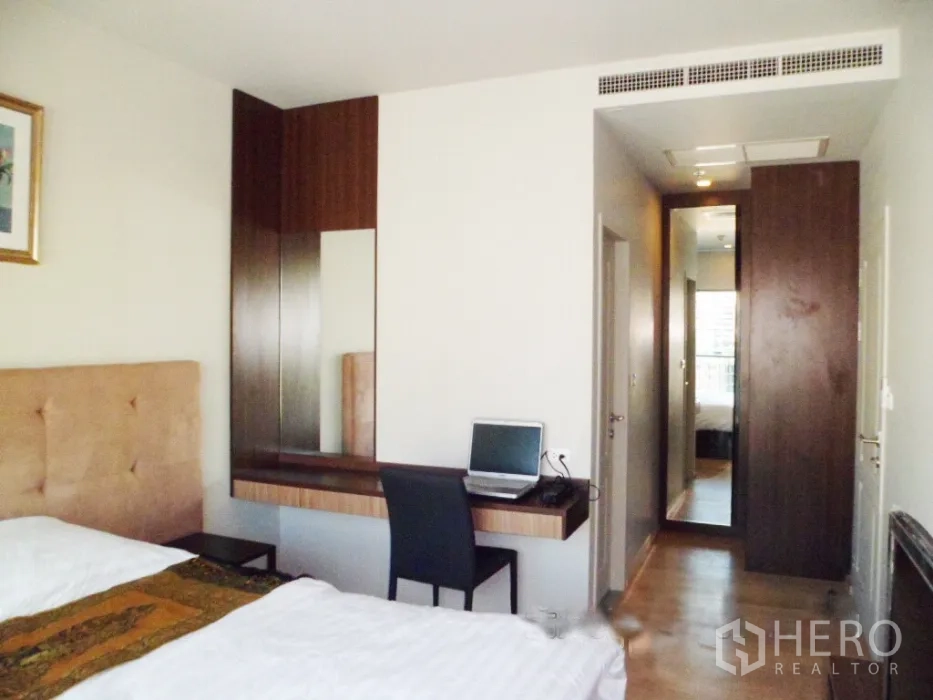 公寓 出租在Bangkok - 次卧配软包床头、内置书桌与木质柜体，走廊尽头设全身镜。