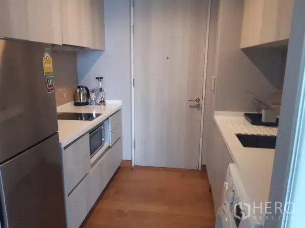 Condominium for rent in Khlong Toei, Bangkok - Compact galley kitchen with built-in cabinets, fridge and electric hob.