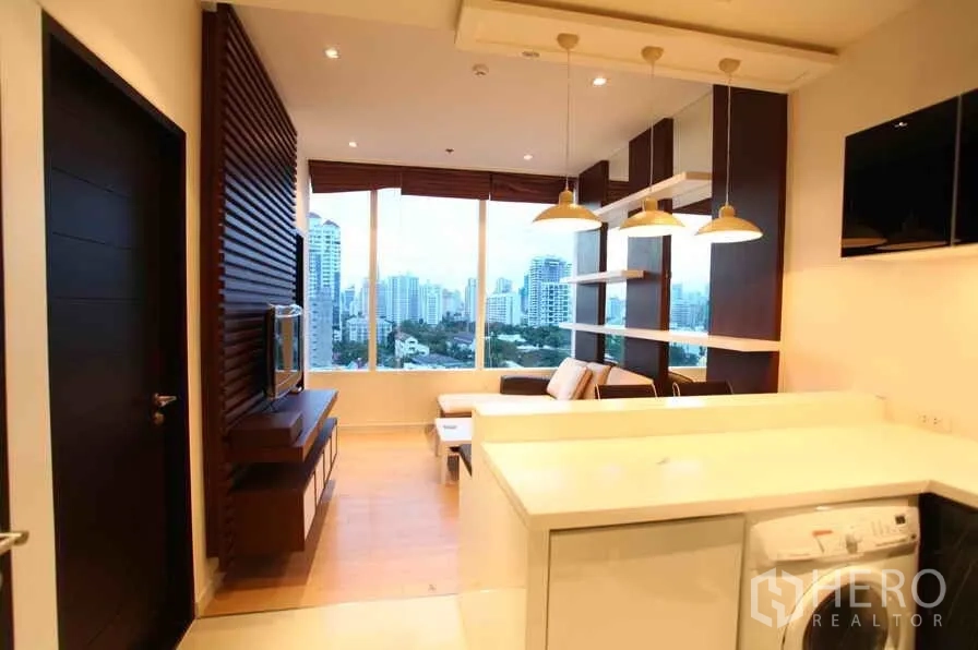 公寓 出租在Watthana, Bangkok - 客餐厨一体空间，吊灯设计，落地窗外为曼谷天际线景观。