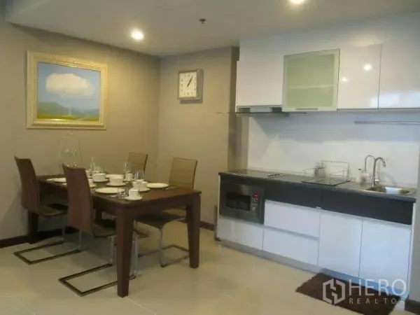 Condominium for rent or sale in Huai Khwang, Bangkok - Open-plan kitchen with white cabinetry, built-in hob and microwave, next to a four-seat dining table and wall art.