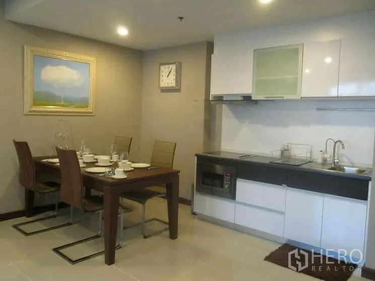 Condominium for rent or sale in Huai Khwang, Bangkok - Open-plan kitchen with white cabinetry, built-in hob and microwave, next to a four-seat dining table and wall art.