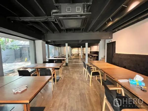 Retail Space for rent in Bangkok - Long open-plan dining hall with wooden tables, a black ceiling and wide windows.