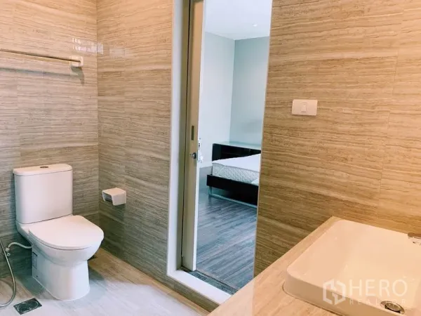 公寓 出租在Watthana, Bangkok - 浅色调卫浴，马桶与洗手台，滑门通向卧室。