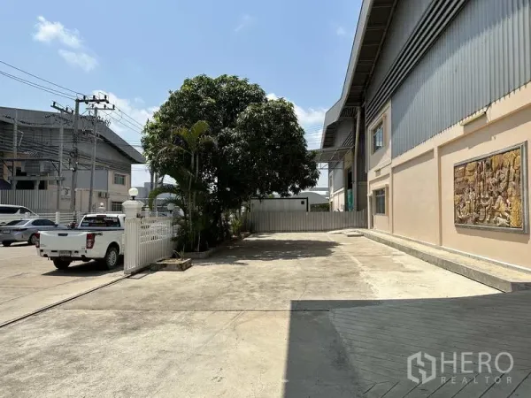 โรงงาน ให้เช่า - ทางข้างอาคารพร้อมรั้วสีขาว ต้นไม้ให้ร่ม และพื้นที่กลับรถสำหรับรถบรรทุก