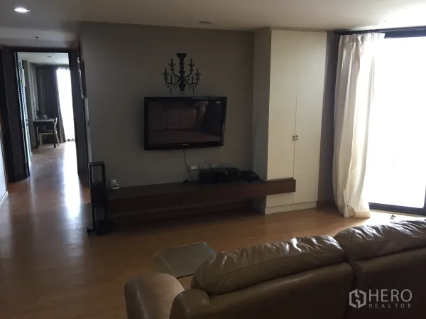 公寓 出租在Watthana, Bangkok - 起居区设壁挂电视与长电视柜，落地窗配窗帘，木地板温暖舒适。