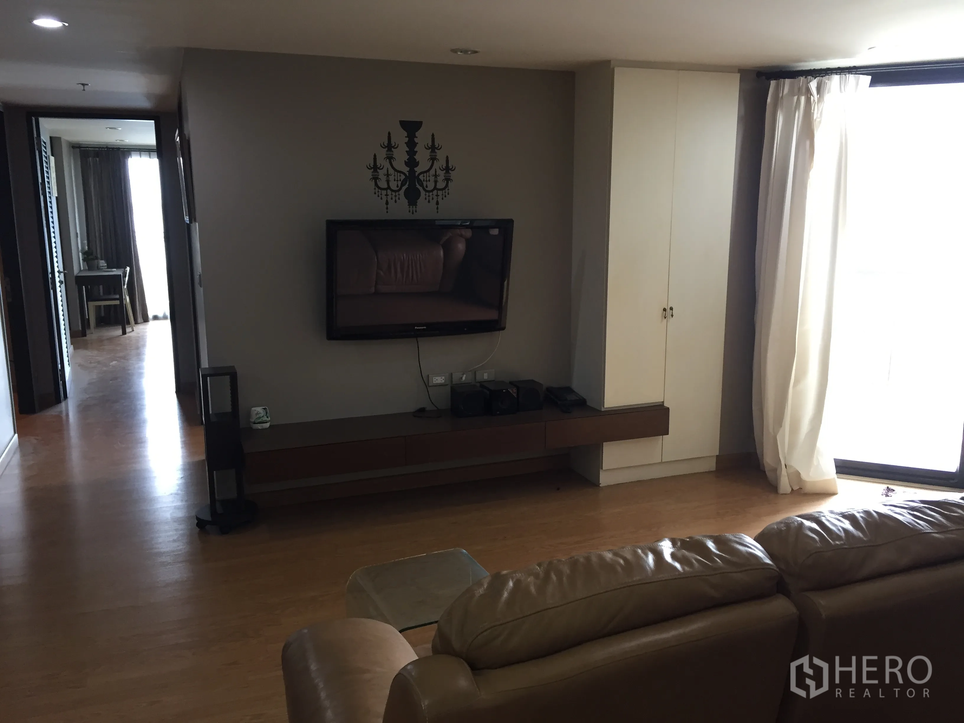 公寓 出租在Watthana, Bangkok - 起居区设壁挂电视与长电视柜，落地窗配窗帘，木地板温暖舒适。