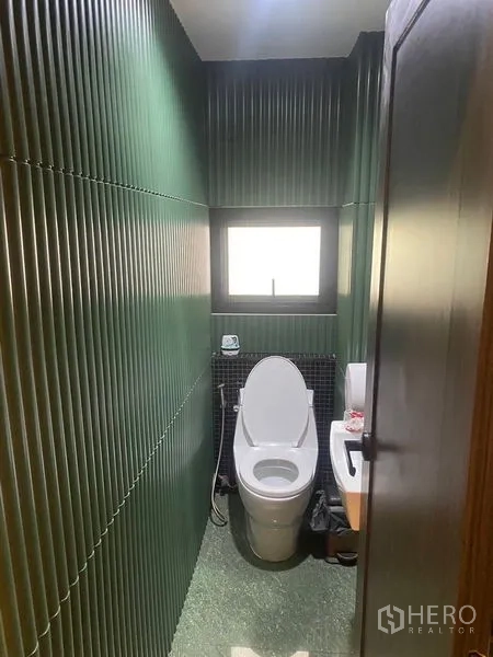 Shophouse for rent - Compact restroom with green ribbed wall panels, window, and modern toilet.
